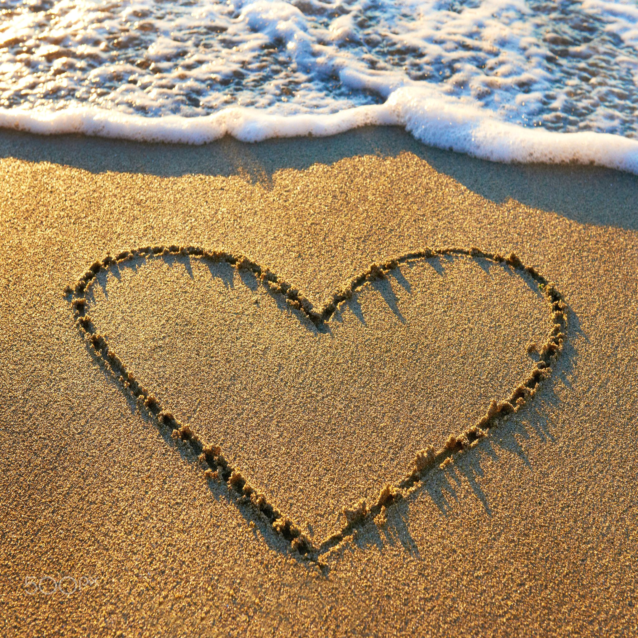 heart drawn on the beach sand with sea foam and wave