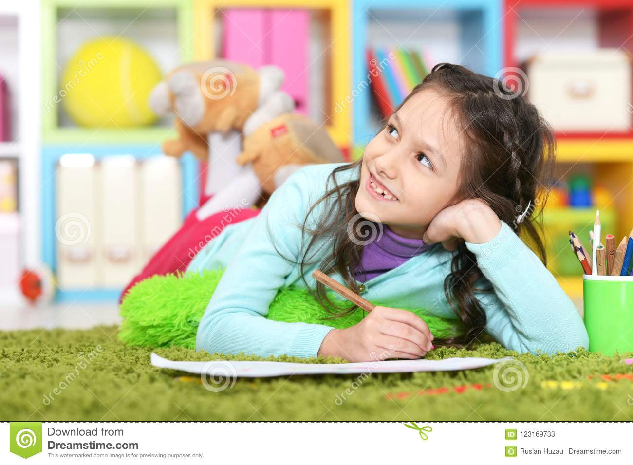 cute little girl drawing while lying on floor on green carpet at home