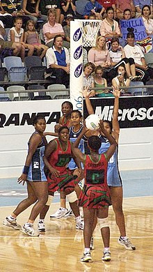 six players in front of a netball basket one is in the act of shooting