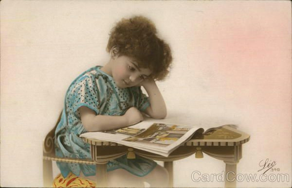 a young child sitting at a desk reading a magazine