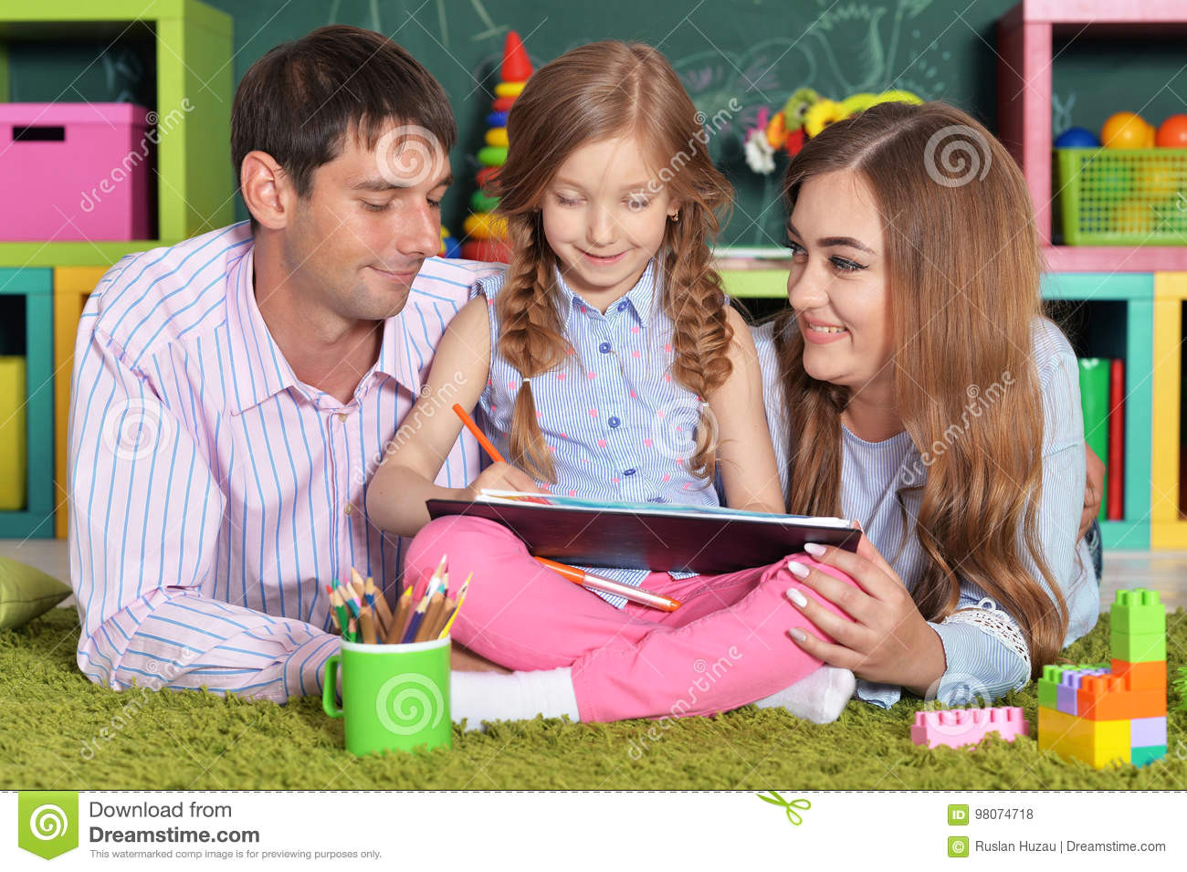 little girl plaits drawing sitting floor her parents lying nearby 98074718 jpg